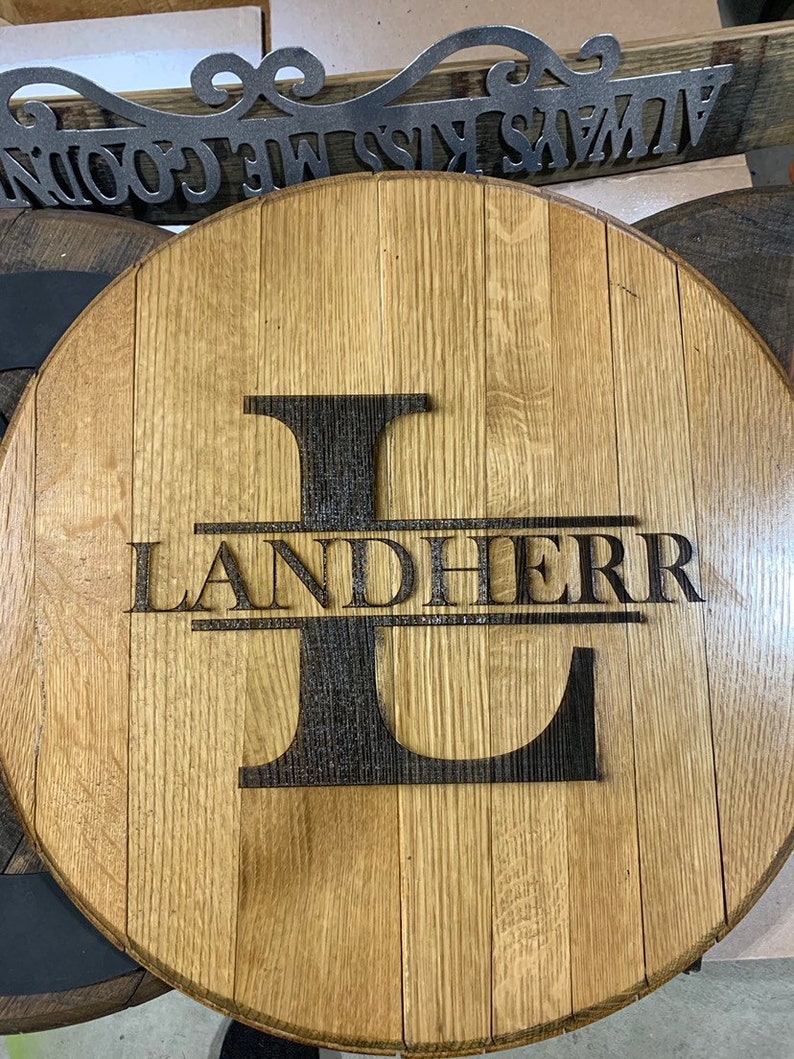 May include: A round wooden sign with the letter L and the name Landherr burned into the wood. The sign is made from a repurposed barrel.