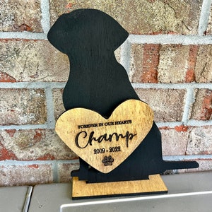 以下が含まれることがあります： 「Forever in our hearts Champ 2009 - 2022」と刻まれたハート型のプレートと、足跡がついた黒い木製の犬のシルエット
