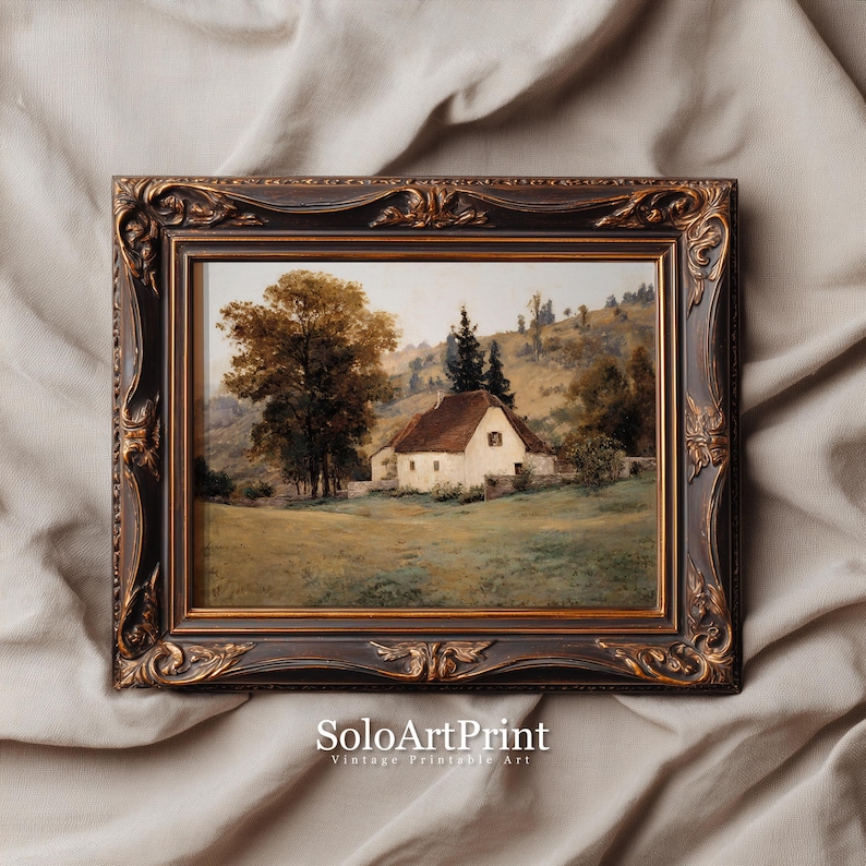 May include: A landscape painting in a dark brown ornate frame with gold accents. The artwork depicts a white cottage with a brown roof nestled in a grassy field, surrounded by large trees and rolling hills under a soft, light-colored sky.
