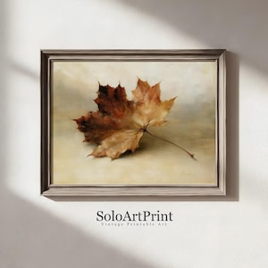 May include: A framed wall art print featuring a single dried maple leaf in shades of brown, orange, and tan against a neutral background. The artwork is enclosed in a textured gray frame. Below the frame, the text SoloArtPrint is visible.