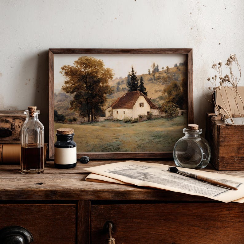 May include: A framed landscape painting depicting a white cottage with a brown roof nestled in a grassy field with large trees and rolling hills. The artwork is displayed alongside glass bottles, a paintbrush, and aged paper on a wooden surface.