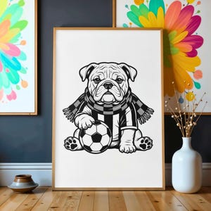 May include: Black and white illustration of a bulldog wearing a soccer jersey and scarf, holding a soccer ball. The artwork is framed in a wooden frame and displayed on a wooden surface. The image has a clean, modern aesthetic.