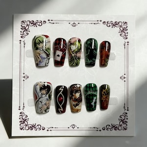 May include: A set of ten false nails with anime-style character art. The nails feature various designs, including character portraits, playing card motifs, and text. Colors include green, red, black, and white. The nails are arranged on a decorative card.