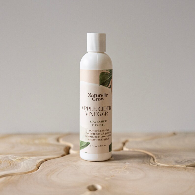 Puede incluir: Una botella blanca de limpiador de espuma baja de vinagre de sidra de manzana Naturelle Grow. La botella est&aacute; etiquetada con un dise&ntilde;o de hoja verde y el texto "Naturelle Grow Vinagre de sidra de manzana Limpiador de espuma baja Combinaci&oacute;n de hierbas potente que apoya el crecimiento saludable del cabello para un cabello m&aacute;s largo y saludable 250 ml (8 fl oz)"