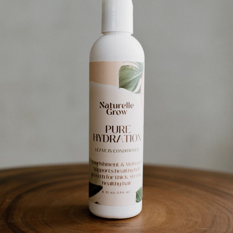 Puede incluir: Una botella blanca de acondicionador sin enjuague etiquetada como "Naturelle Grow Pure Hydration". La botella tiene un dise&ntilde;o de hoja verde y el texto "Nourishment & Moisture Supports healthy hair growth for thick, strong healthy hair 8 fl oz 250 ml".