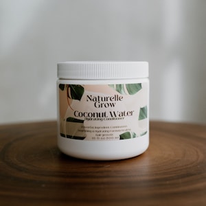 Op de afbeelding: Witte plastic fles met Naturelle Grow Coconut Water Hydrating Conditioner. Het etiket heeft een groen tropisch bladontwerp en de tekst "Powering Ingredient Combination Nourishing & Hydrating Formula Healthy Hair Growth 16 fl oz - 500 ml".