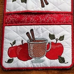 May include: Two quilted pot holders with a red and white floral design. Each pot holder features a mug of hot chocolate with cinnamon sticks and red apples.