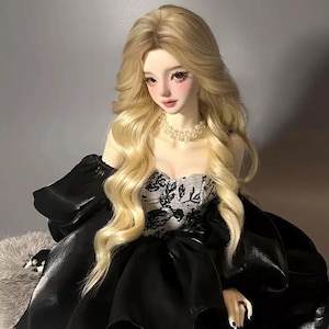 May include: A doll with long, wavy blonde hair and a pearl necklace. The doll wears a black satin gown with a white and black lace bodice. The doll has rosy cheeks and lips, and is set against a neutral background.
