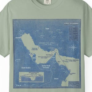 Może przedstawiać: Jasnozielona koszulka z niebieską mapą Bliskiego Wschodu, w tym Iranu, Arabii Saudyjskiej i Zjednoczonych Emiratów Arabskich. Koszulka ma okrągły dekolt i krótkie rękawy.