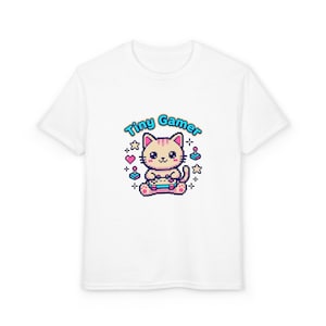 Puede incluir: Camiseta blanca con un diseño de gato pixelado sosteniendo un mando de videojuegos. El texto "Tiny Gamer" es azul, con corazones, estrellas e iconos de consola. La camiseta está hecha de un material suave.