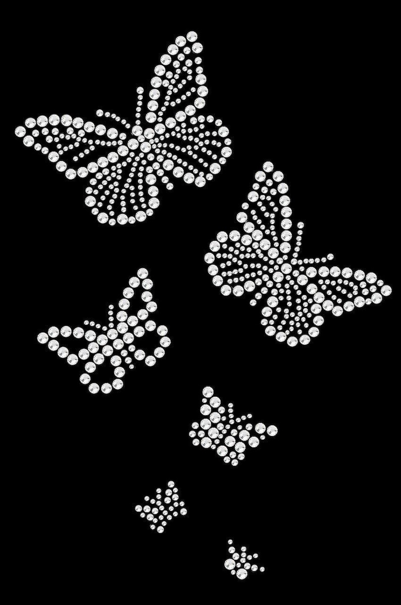K&ouml;nnte beinhalten: Auf schwarzem Hintergrund ein Design aus mehreren Schmetterlingen. Jeder Schmetterling besteht aus zahlreichen kleinen, funkelnden, wei&szlig;en Strasssteinen, die einen schimmernden Effekt erzeugen. Die Schmetterlinge variieren in der Gr&ouml;&szlig;e und sind in einem dynamischen, aufw&auml;rts gerichteten Muster angeordnet.