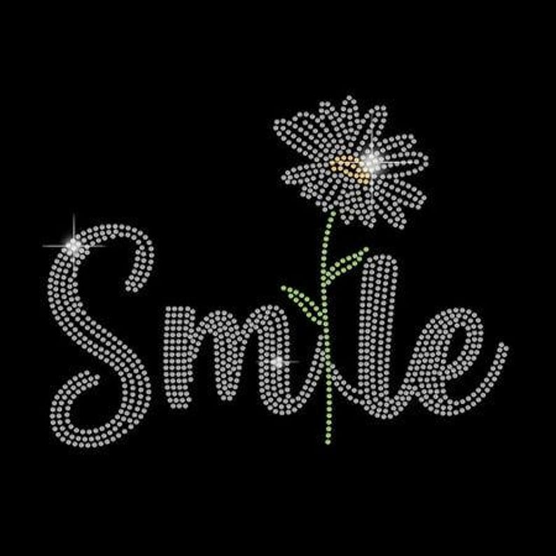 K&ouml;nnte beinhalten: Auf schwarzem Hintergrund steht das Wort "Smile" in glitzernden Strasssteinen. Eine Strass-G&auml;nsebl&uuml;mchen mit gr&uuml;nem Stiel und Bl&auml;ttern befindet sich &uuml;ber dem Buchstaben "e".