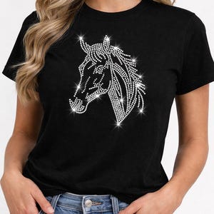 Peut inclure: T-shirt noir avec un motif de tête de cheval en strass étincelants. La tête de cheval est représentée dans un motif détaillé et scintillant, créant un contraste saisissant avec le tissu sombre. Le t-shirt est de style col rond classique.