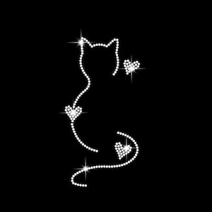 K&ouml;nnte beinhalten: Eine Katzen-Silhouette aus glitzernden Strasssteinen mit drei herzf&ouml;rmigen Akzenten. Der K&ouml;rper und der Schwanz der Katze werden durch eine Reihe kleiner, funkelnder Strasssteine gebildet. Die Herzen sind ebenfalls aus Strass, vor schwarzem Hintergrund.