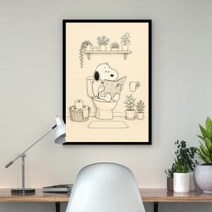 Puede incluir: Impresi&oacute;n enmarcada en negro que muestra a Snoopy sentado en un inodoro, leyendo un peri&oacute;dico. La ilustraci&oacute;n en blanco y negro presenta una estanter&iacute;a con plantas en macetas, una cesta de papel higi&eacute;nico y un rollo de papel higi&eacute;nico. El fondo es neutro.
