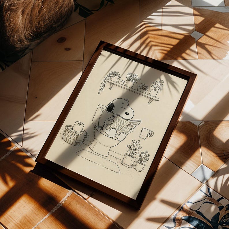 Puede incluir: Ilustraci&oacute;n en blanco y negro enmarcada que muestra a Snoopy sentado en un inodoro, leyendo un peri&oacute;dico. La obra de arte incluye una estanter&iacute;a con plantas en macetas, una cesta de papel higi&eacute;nico y plantas en macetas adicionales. El marco es marr&oacute;n oscuro.