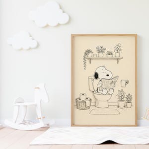 Puede incluir: Ilustraci&oacute;n en blanco y negro enmarcada de Snoopy leyendo un peri&oacute;dico en el inodoro. La obra de arte representa una escena de ba&ntilde;o, con una estanter&iacute;a de plantas y una cesta de papel higi&eacute;nico.