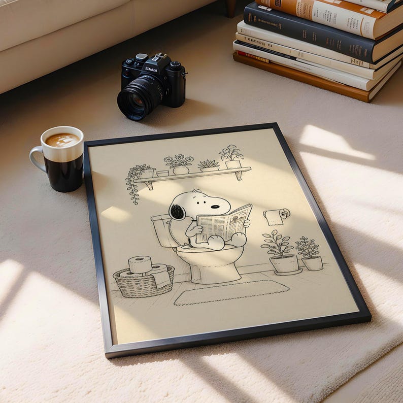 Puede incluir: Impresi&oacute;n art&iacute;stica en blanco y negro enmarcada de Snoopy. Snoopy est&aacute; sentado en un inodoro leyendo un peri&oacute;dico. La impresi&oacute;n art&iacute;stica est&aacute; rodeada de plantas en macetas y un rollo de papel higi&eacute;nico. Una c&aacute;mara y una taza de caf&eacute; tambi&eacute;n est&aacute;n en la imagen.