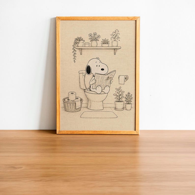 Puede incluir: Ilustraci&oacute;n en blanco y negro enmarcada de Snoopy leyendo el peri&oacute;dico en el inodoro. La imagen incluye plantas, una estanter&iacute;a y papel higi&eacute;nico. La obra de arte est&aacute; en un marco de madera.