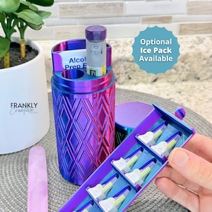May include: A cylindrical, iridescent purple and blue storage case with a diamond-patterned exterior. The case features an open top compartment holding an alcohol prep pad and a medication pen, plus a hinged side tray containing six needle tips.