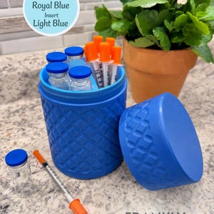 May include: A royal blue cylindrical container with a textured geometric pattern and a light blue interior insert. The container holds several clear glass vials with blue caps and syringes with orange caps. A matching lid sits beside it.