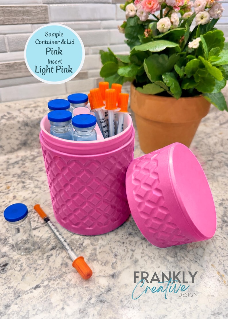 May include: A pink cylindrical container with a textured diamond pattern and a light pink insert, accompanied by a matching lid. The container holds several small glass vials with blue caps and syringes with orange caps, with one additional vial and syringe nearby.