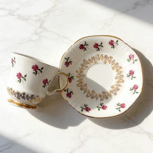 Peut inclure: Service à thé vintage en porcelaine blanche orné de roses roses et de détails dorés. La tasse a une anse en forme de cœur et un pied doré. L'assiette présente un motif floral doré.