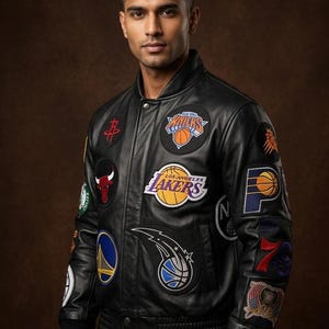 Op de afbeelding: Zwarte leren bomberjack met meerdere NBA-teampatches, waaronder de Lakers, Bulls en Knicks. De jas heeft een geribbelde kraag, manchetten en zoom. De patches zijn in verschillende kleuren en tonen teamlogo's en -namen.
