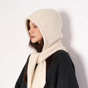 May include: Cream-colored knit hood and scarf set. The hood is designed with a ribbed texture and a built-in scarf that drapes around the neck. The scarf is a matching cream color and is made of a soft, warm material. The set is perfect for cold weather.