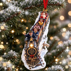 May include: A Christmas tree ornament shaped like a train with the text The Polar Express, Taylor, and 2026. The train features a conductor holding a ticket that says BELIEVE, passengers in the cars, and Santa Claus at the back, all on snowy tracks.