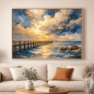 Puede incluir: Pintura al óleo de un muelle que se extiende hacia el océano bajo un cielo dramático. La obra de arte presenta un muelle de madera, agua azul agitada y un cielo lleno de nubes doradas y azules. La pintura está enmarcada en un marco de madera de color claro.