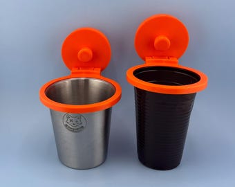 Può includere: Due portabicchieri con bordi in plastica arancione brillante e coperchi attaccati. Il supporto a sinistra è in acciaio inossidabile spazzolato con un piccolo logo a forma di volpe e il testo Lisek Studio. Quello a destra è in plastica marrone.