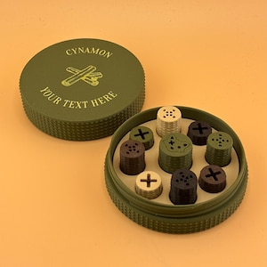 May include: An olive green container with a screw-top lid and a matching base. The lid is labelled "CYNAMON" with a cinnamon stick graphic and "YOUR TEXT HERE". Inside, are various coloured cylindrical objects with cross and dot designs.