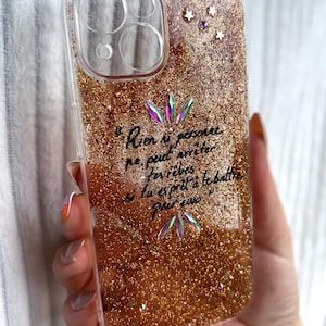 Peut inclure: Coque de téléphone transparente avec un design de paillettes dorées. La coque présente une citation en français et est ornée de pierres précieuses irisées et d'étoiles. Conçu pour un smartphone.