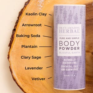 Puede incluir: Un envase cil&iacute;ndrico de polvos corporales con un dise&ntilde;o floral de lavanda, etiquetado como "ORA'S AMAZING HERBAL BODY POWDER". El envase enumera ingredientes como arcilla de caol&iacute;n, arrurruz y lavanda. El producto es de 71 g.