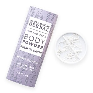 Puede incluir: Un envase cil&iacute;ndrico de polvos corporales y un peque&ntilde;o recipiente con polvos. El envase es de color lavanda con un estampado floral y el texto "ORA'S AMAZING HERBAL BODY POWDER BLISSFUL EARTH." El envase es de 71g.