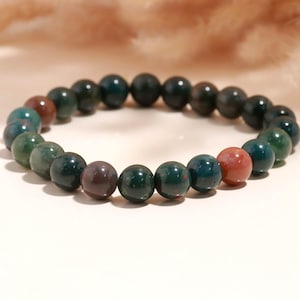 May include: A bracelet made of dark green and red-brown speckled stone beads. The beads are round and strung together to form a bracelet. The bracelet is a natural stone accessory, suitable for everyday wear.