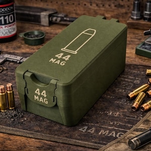 May include: An olive green ammunition box with the text "44 MAG" and a bullet graphic. Several brass bullets are scattered around the box. A bottle of Hoddon H110 pistol powder is visible in the background.