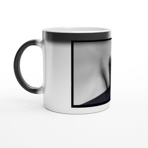 Könnte beinhalten: Weißer, farbwechselnder Keramikbecher. Die Außenseite des Bechers wechselt von Schwarz zu Weiß, wenn eine heiße Flüssigkeit hinzugefügt wird. Auf dem Becher ist ein Schwarz-Weiß-Bild aufgedruckt. Der Becher hat einen schwarzen Griff.