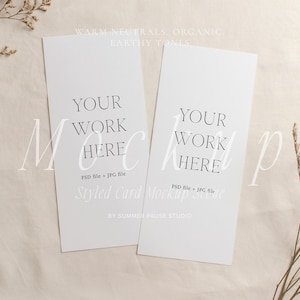 May include: Two white rectangular cards with the text "YOUR WORK HERE" are displayed on a beige fabric surface. The cards also include the text "PSD file + JPG file" and "Styled Card Mockup Studio". Dried floral elements are arranged around the cards.