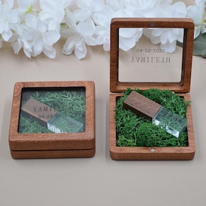 May include: Two square wooden boxes with clear lids, each containing green moss and a wooden and clear acrylic USB drive. The lids are engraved with the name YAMILETH and the date 04-25-2026. The boxes feature a natural wood grain finish.