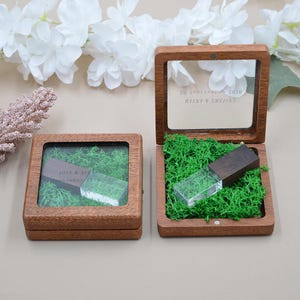 May include: Two square wooden boxes with clear lids, each containing bright green preserved moss and a dark wood and clear acrylic USB flash drive. The lids are engraved with names and dates, including JOSE & ALEXANDRA and MAYRA & EMANUEL.