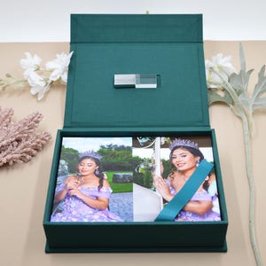 Può includere: Una scatola portaricordi rettangolare verde scuro con chiusura magnetica, contenente due stampe fotografiche di una persona che indossa un abito floreale color lavanda e un diadema. La scatola presenta un dettaglio rettangolare argentato sul coperchio interno.