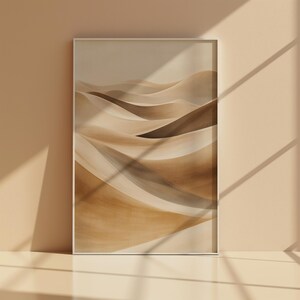 Könnte beinhalten: Gerahmter Kunstdruck mit einer abstrakten Wüstenlandschaft. Das Kunstwerk zeigt sich wellenförmige Sanddünen in Beige-, Braun- und Brauntönen. Der Druck wird in einem weißen Rahmen mit Schatten von einem Fenster präsentiert.