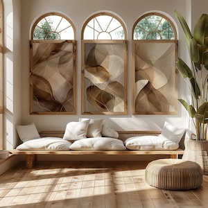 Könnte beinhalten: Drei gerahmte abstrakte Kunstwerke in Braun- und Beigetönen hängen über einer Holzbank mit weißen Kissen. Der Raum verfügt über Bogenfenster, einen gewebten Ottomanen und eine große Topfpflanze, die eine warme, einladende Atmosphäre schaffen.