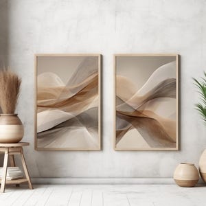 Könnte beinhalten: Zwei rechteckige gerahmte Wandbilder mit abstrakten, fließenden Wellen in Beige-, Braun- und Dunkelgrautönen. Die Bilder hängen nebeneinander an einer Wand, ergänzt durch einen Holzhocker, eine Keramikvase mit Trockengras und zwei Bodenvasen.