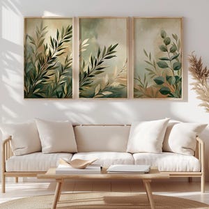 Könnte beinhalten: Ein Set aus drei gerahmten Wandbildern mit botanischen Illustrationen von grünen Blättern und Zweigen vor einem weichen, gedämpften Hintergrund in Beige- und Salbeitönen. Die Kunstwerke sind in hellen Holzrahmen an einer weißen Wand montiert.