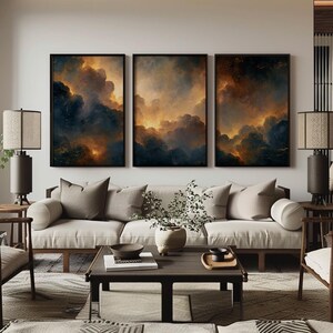 Könnte beinhalten: Ein Triptychon aus gerahmter Wandkunst mit dunklen, dramatischen Wolken, die von goldenem Licht beleuchtet werden, platziert über einem beigen Sofa mit passenden Kissen, einem Couchtisch aus Holz und zwei Lampen mit zylindrischen Stoffschirmen.