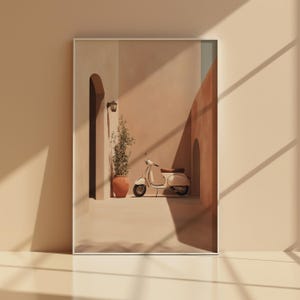 Könnte beinhalten: Gerahmter Kunstdruck mit einem cremefarbenen Vintage-Roller in einer sonnigen Gasse. Die Szene umfasst einen Terrakottatopf mit einer Pflanze, einen gewölbten Durchgang und eine Wandlampe, alles in warmen, erdigen Tönen.