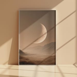 Könnte beinhalten: Ein gerahmter Kunstdruck mit einer ruhigen Landschaft unter einem Halbmond. Das Kunstwerk zeigt eine gedämpfte Farbpalette aus Beige, Braun und Hellbraun mit einer detaillierten Darstellung von Bergen, Feldern und einem Himmelskörper.